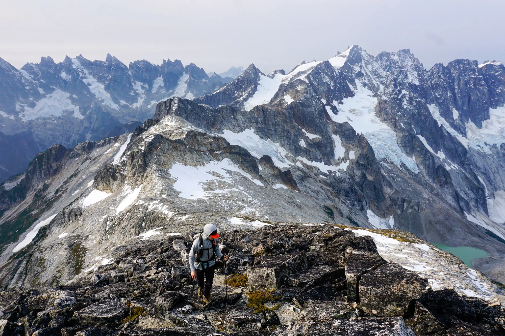 A lone climber standing on a sharp, snowy mountain peak under a clear blue sky.