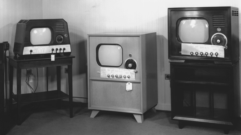 An array of vintage black and white console television sets housed in heavy wooden cabinets.
