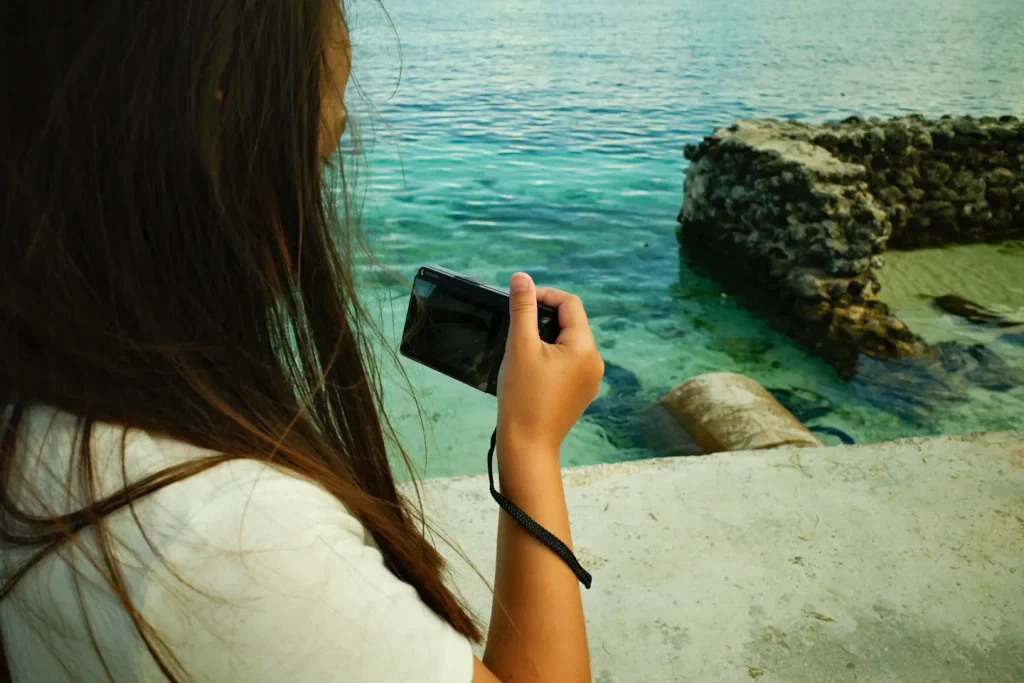 A woman using a compact camera to take a photo of a tropical ocean scene.