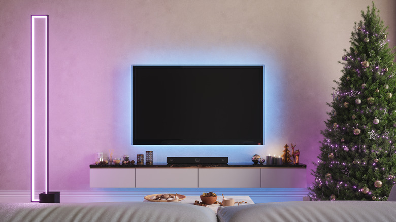 A television in a dark room with soft ambient backlighting and a Christmas tree in the background.