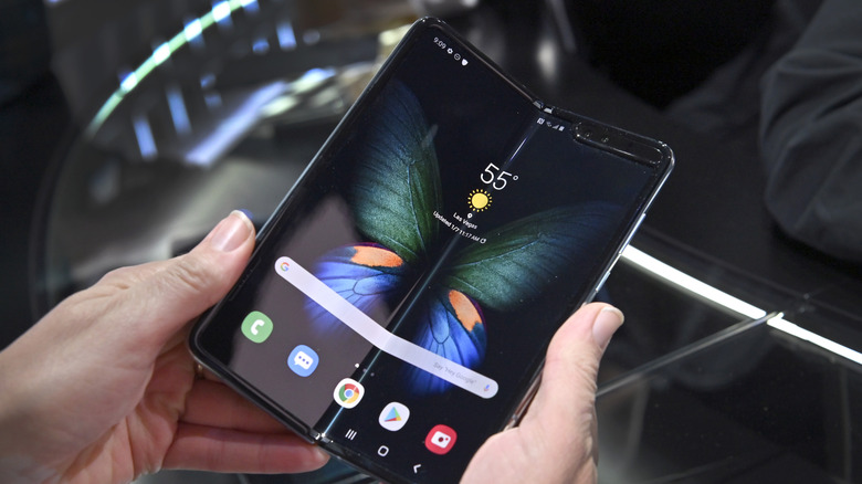 Hand holding a first-generation Samsung Galaxy Fold showing a prominent vertical crease in the center of the display.