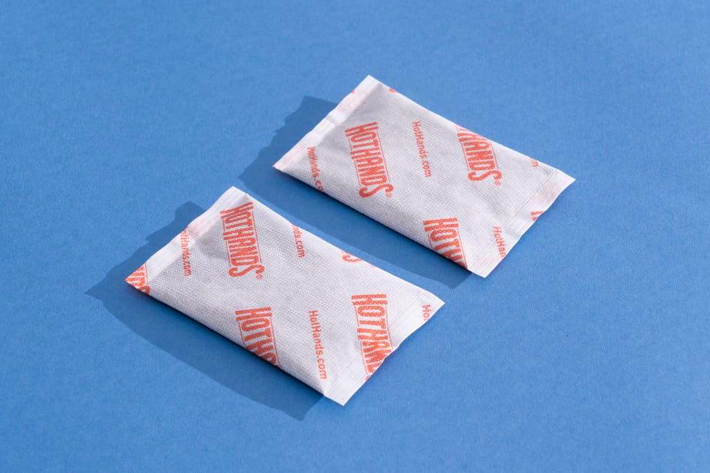 Two HotHands disposable chemical hand warmers on a blue background.