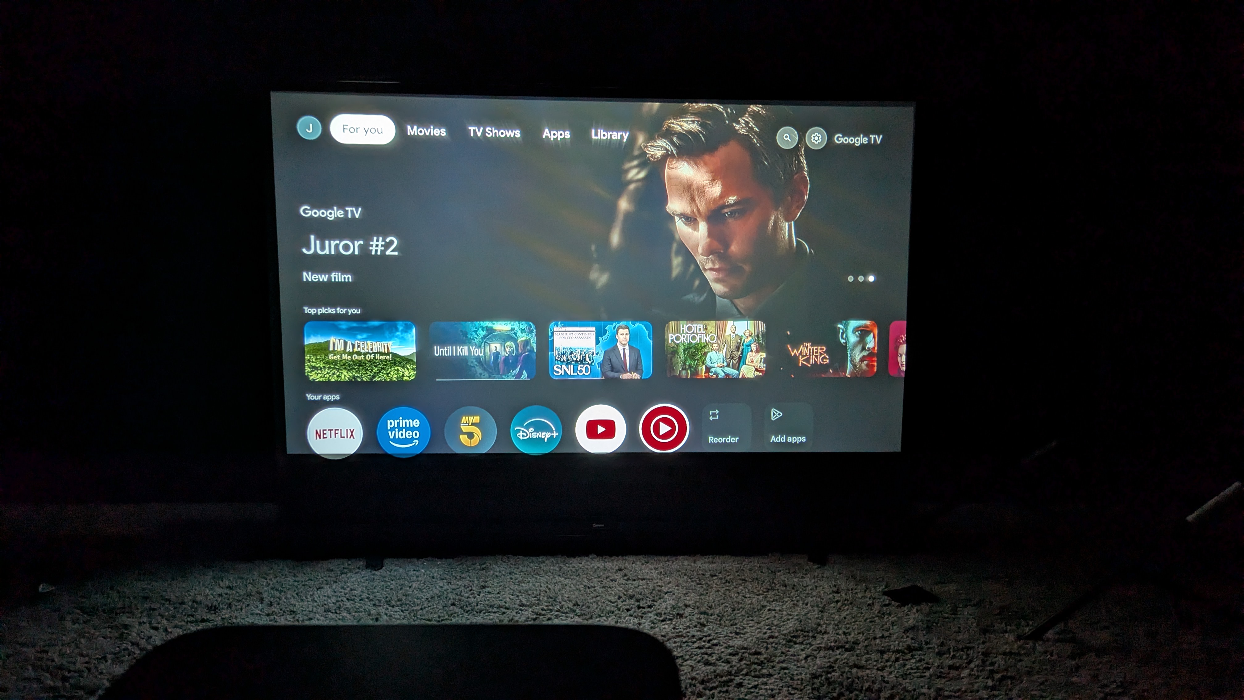 The Yaber K3 projector displaying the Google TV home screen interface with various streaming apps.