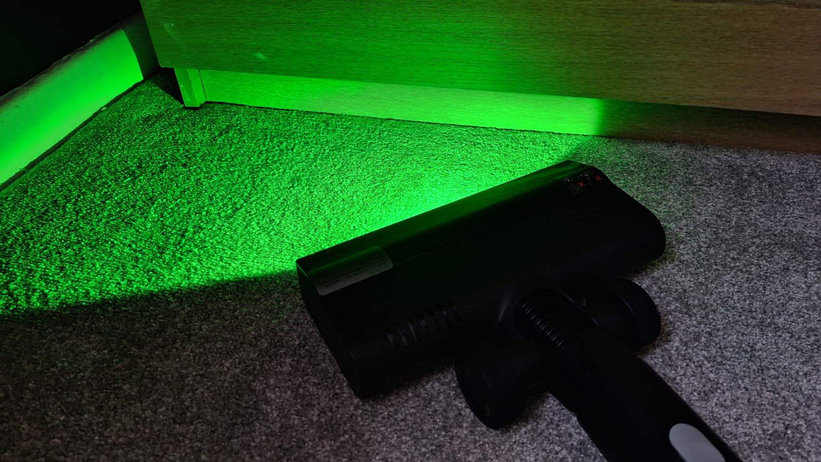Green laser light from the Roborock H60 floorhead illuminating dust particles on a dark floor.