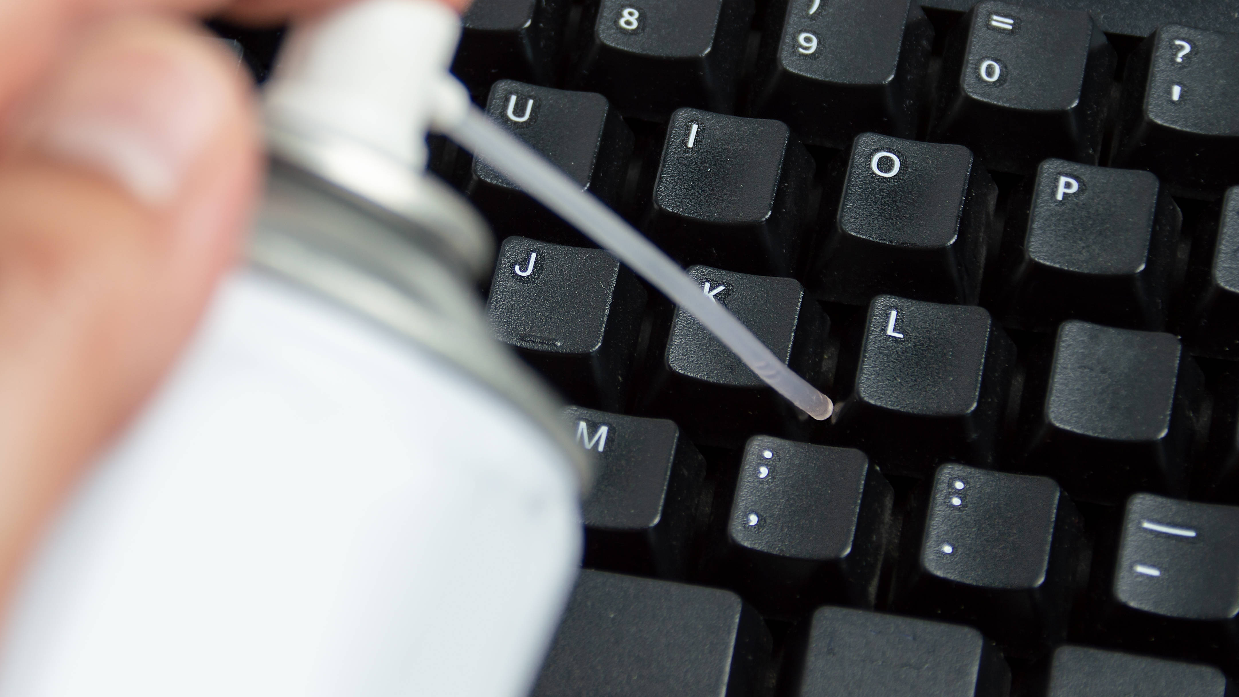 Hand using a canister of compressed air to clean a computer keyboard.