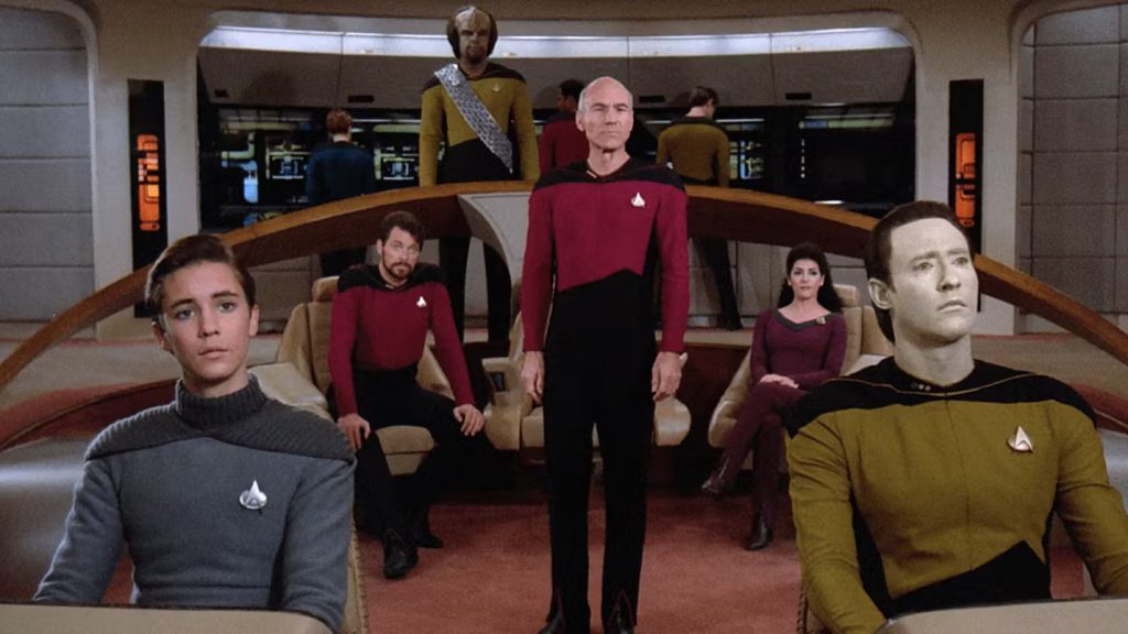 The main cast of Star Trek: The Next Generation standing on the bridge of the USS Enterprise-D.