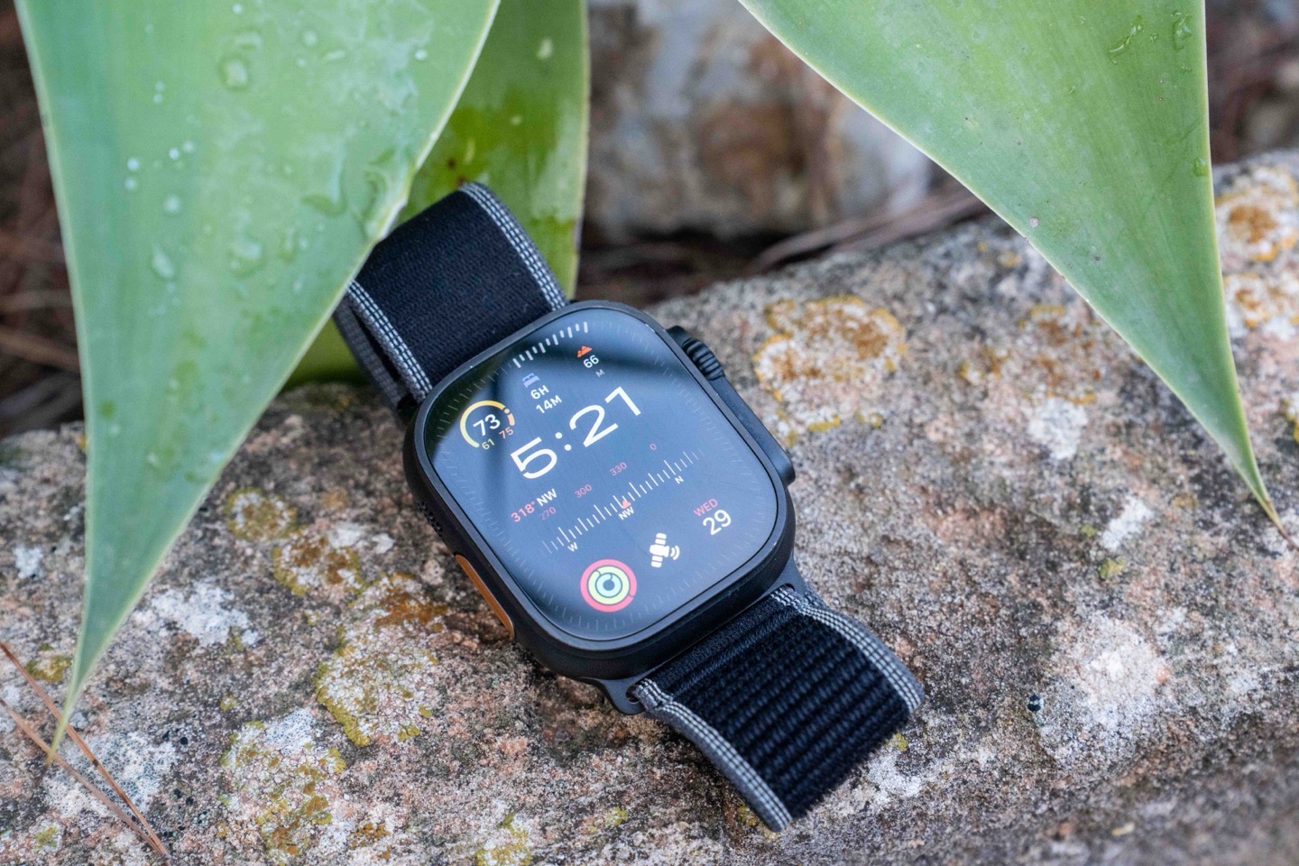 The Apple Watch Ultra 3 resting on a rock in a mountainous outdoor setting.