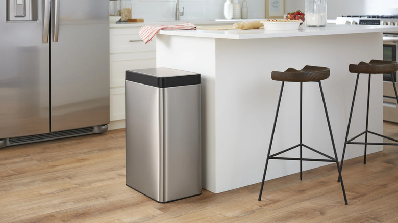 A stainless steel Kohler motion sensor trash can placed next to a white kitchen island.