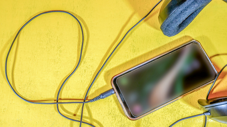 Wired headphones being plugged into a smartphone's 3.5mm jack against a yellow background.