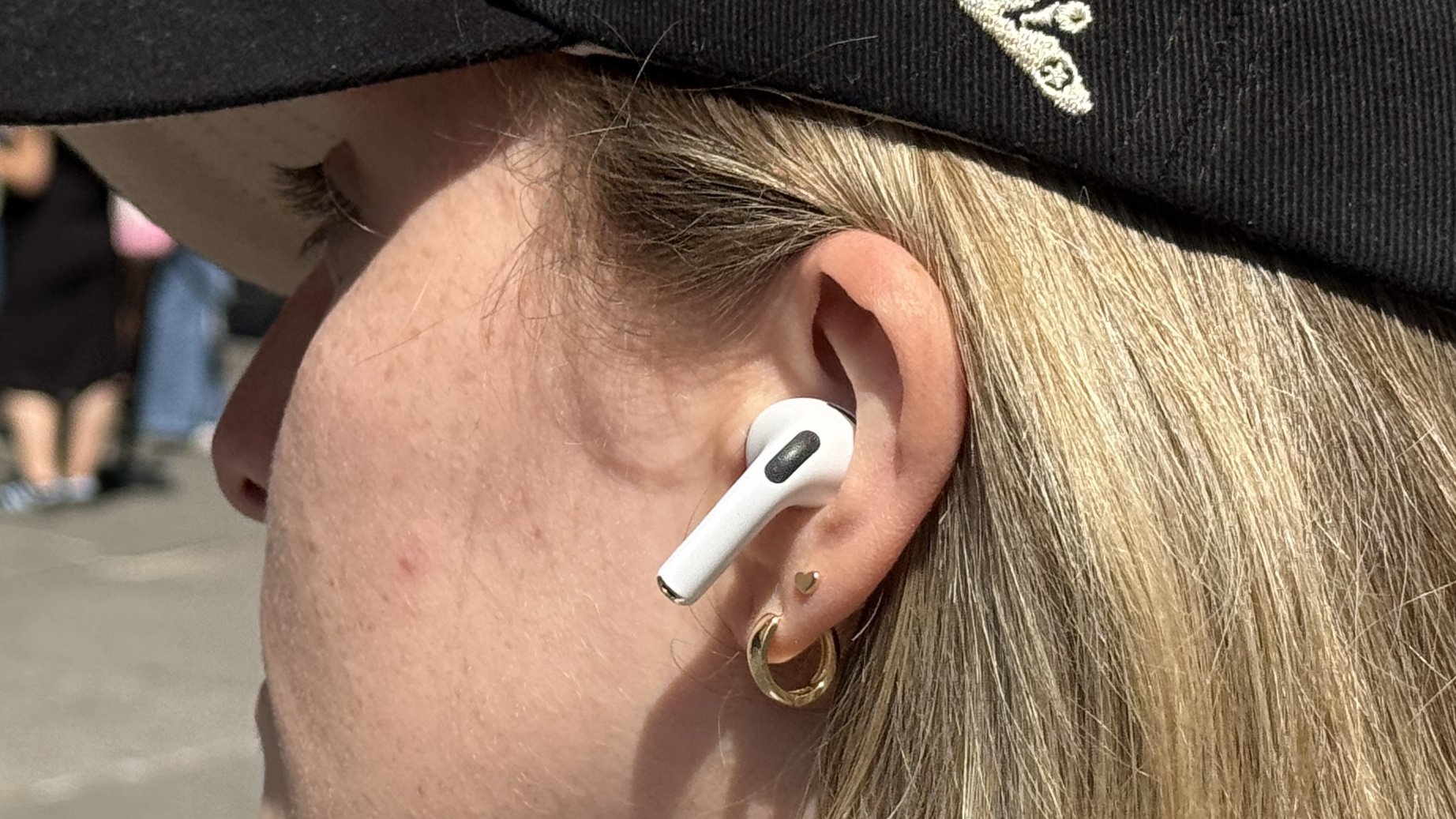 A woman wearing AirPods Pro 3 while walking outdoors in a sunny environment.
