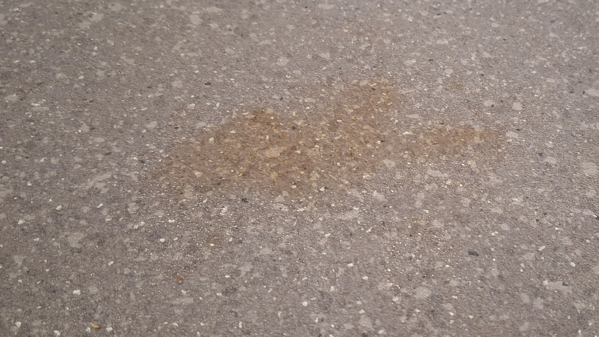 A large, sticky ketchup stain on a floor surface before being cleaned.
