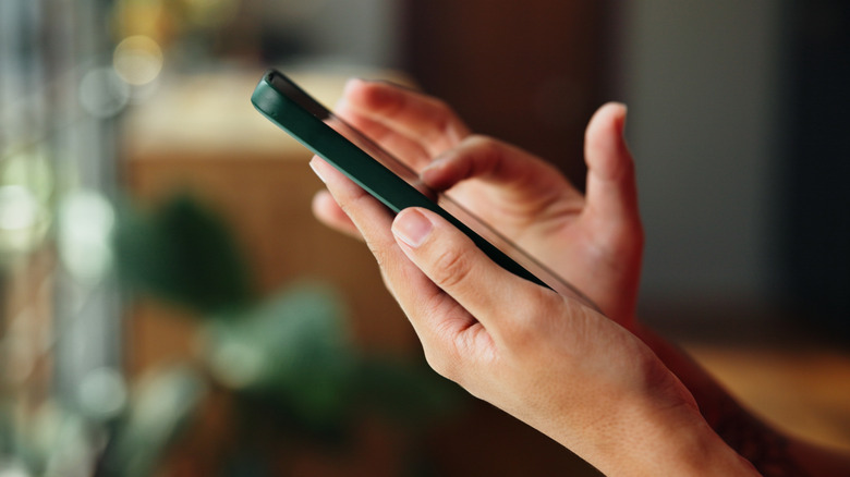 A person comfortably holding a smartphone in a softly lit living room environment.