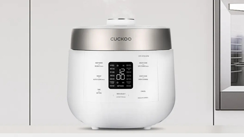 A white Cuckoo Twin Pressure Rice Cooker emitting steam on a countertop.