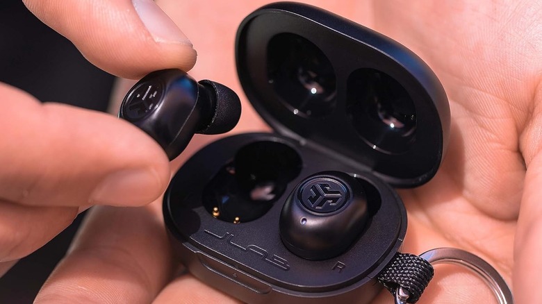 A pair of JLab JBuds Mini wireless earbuds and their tiny charging case held in a person's palm.