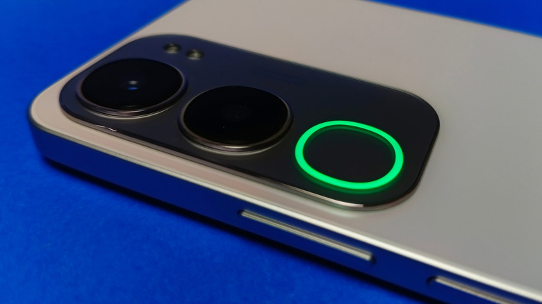 A close-up of a smartphone with a small green LED notification light glowing at the top of the screen.