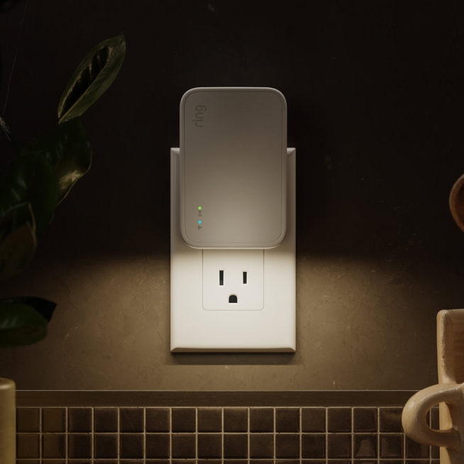 Close-up of a Ring Bridge plugged into a kitchen outlet with its indicator light visible.