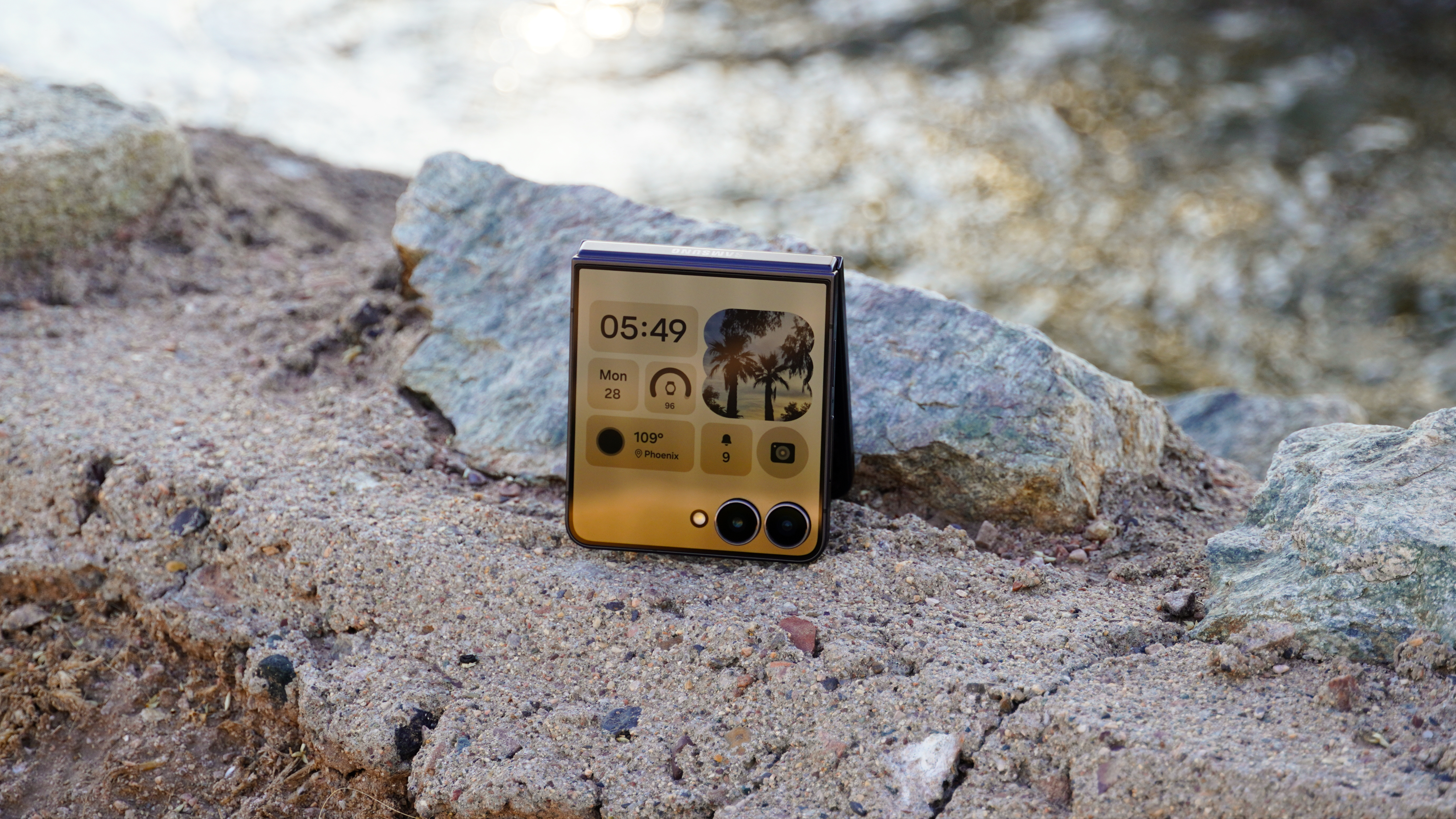 A foldable Samsung Galaxy Z Flip 7 placed on a rock near a flowing stream.