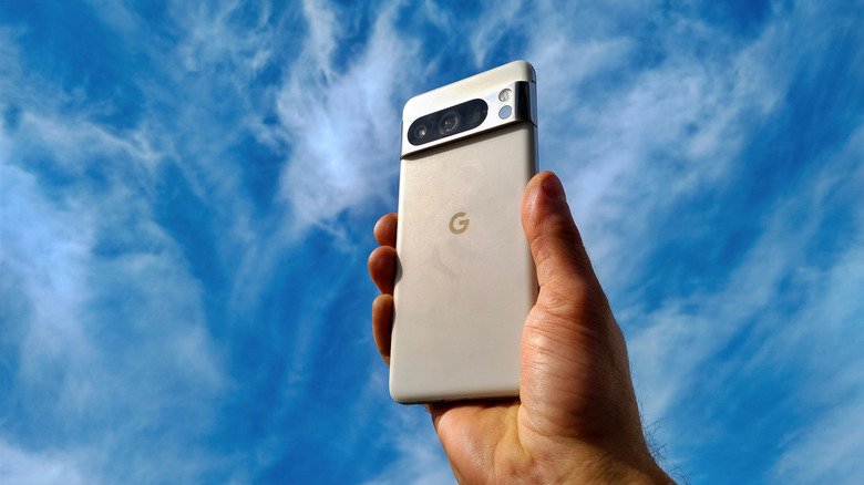 A hand holding a Google Pixel phone against a blue sky background.
