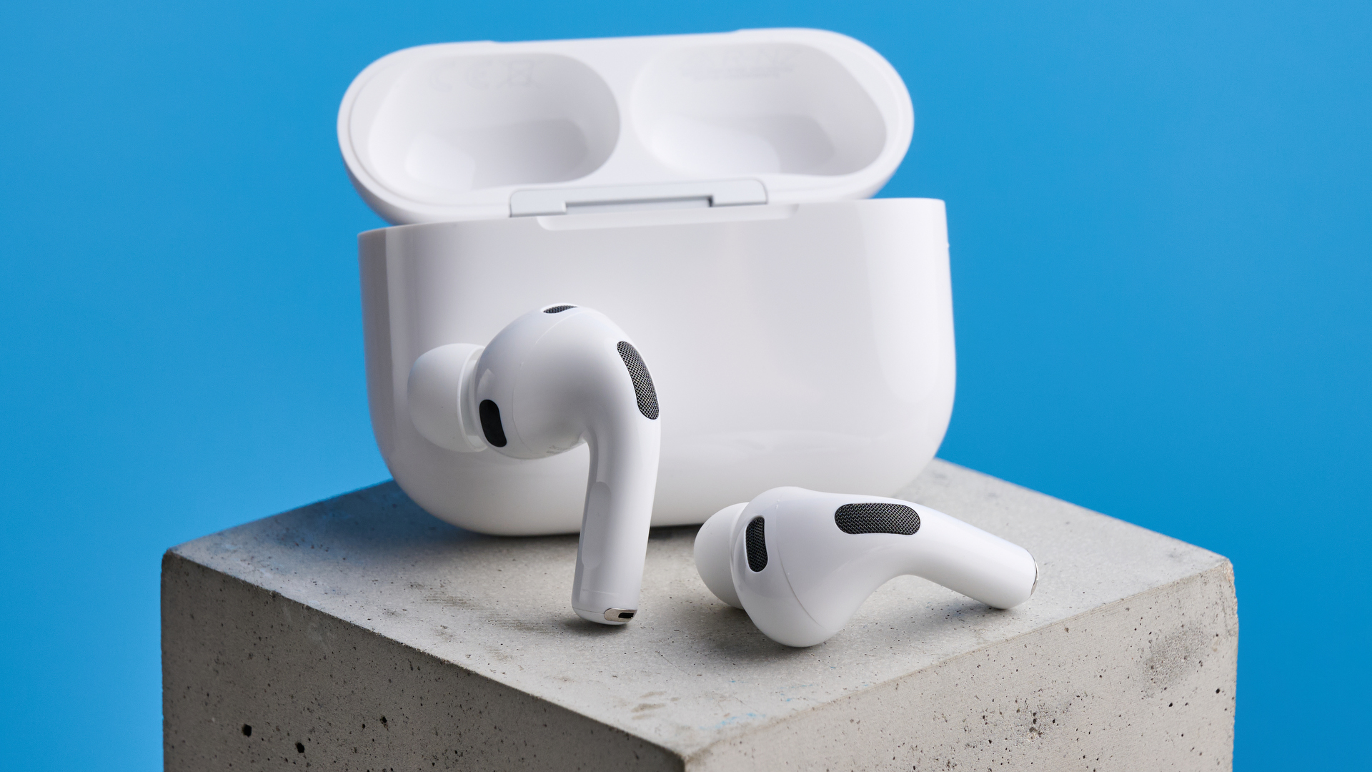 AirPods Pro 3 earbuds lying on a flat white surface next to their charging case.