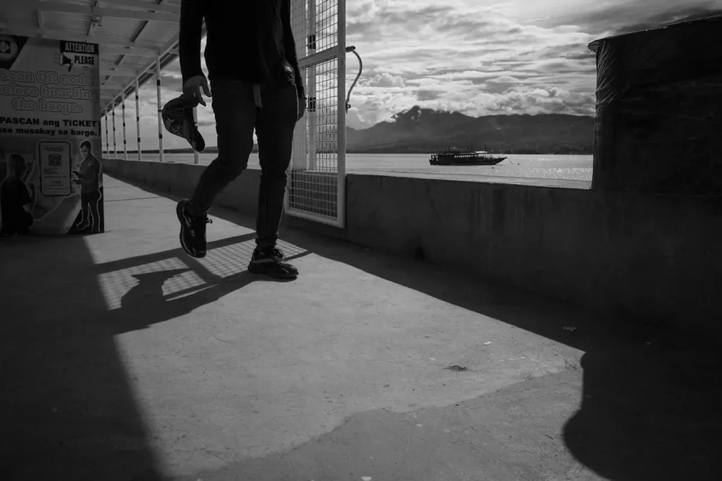 A dramatic black and white street photograph of a silhouette at a port.
