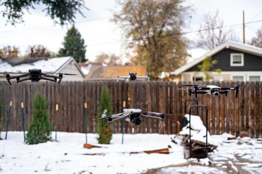Four different DJI drone models hovering together in a snowy environment.