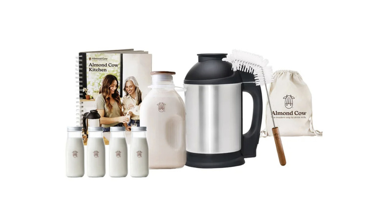 An Almond Cow milk maker machine shown with its accessories and a pitcher of fresh plant-based milk.