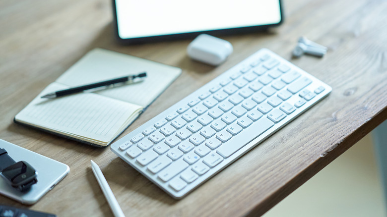 A clean white wireless keyboard sitting on a wooden desk surface.