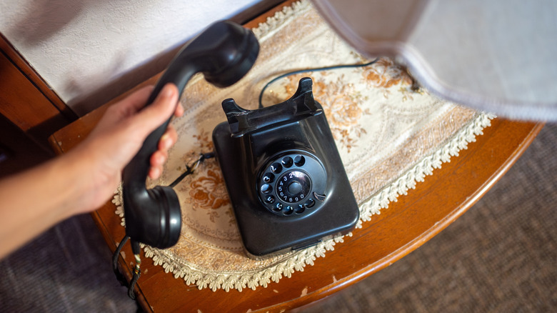 A person's hand lifting the receiver of a classic rotary dial telephone.