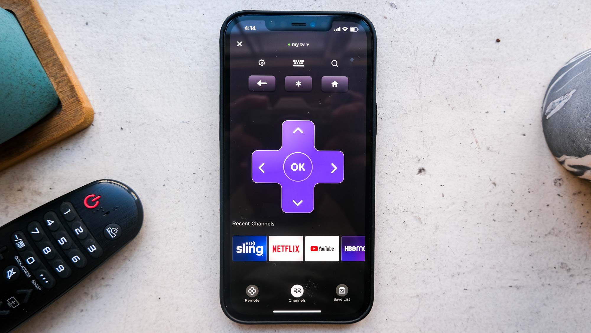 A person holding a smartphone showing the Roku remote control interface.