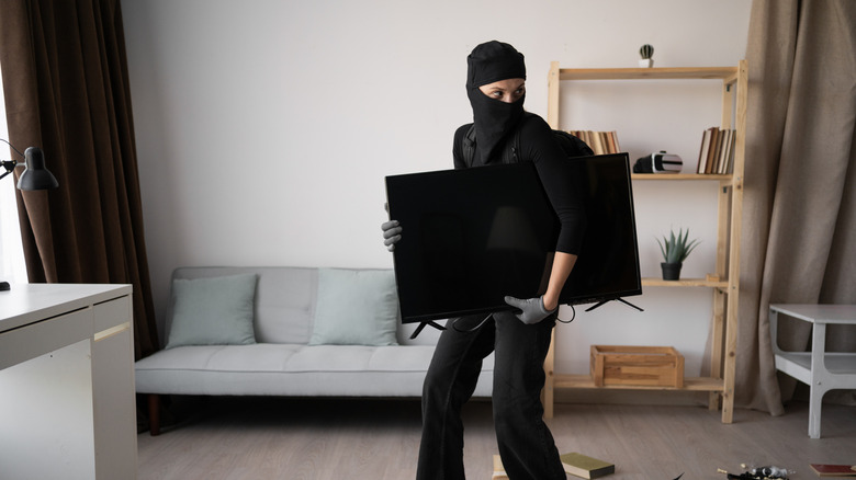 A person in dark clothing attempting to steal a television from a home.