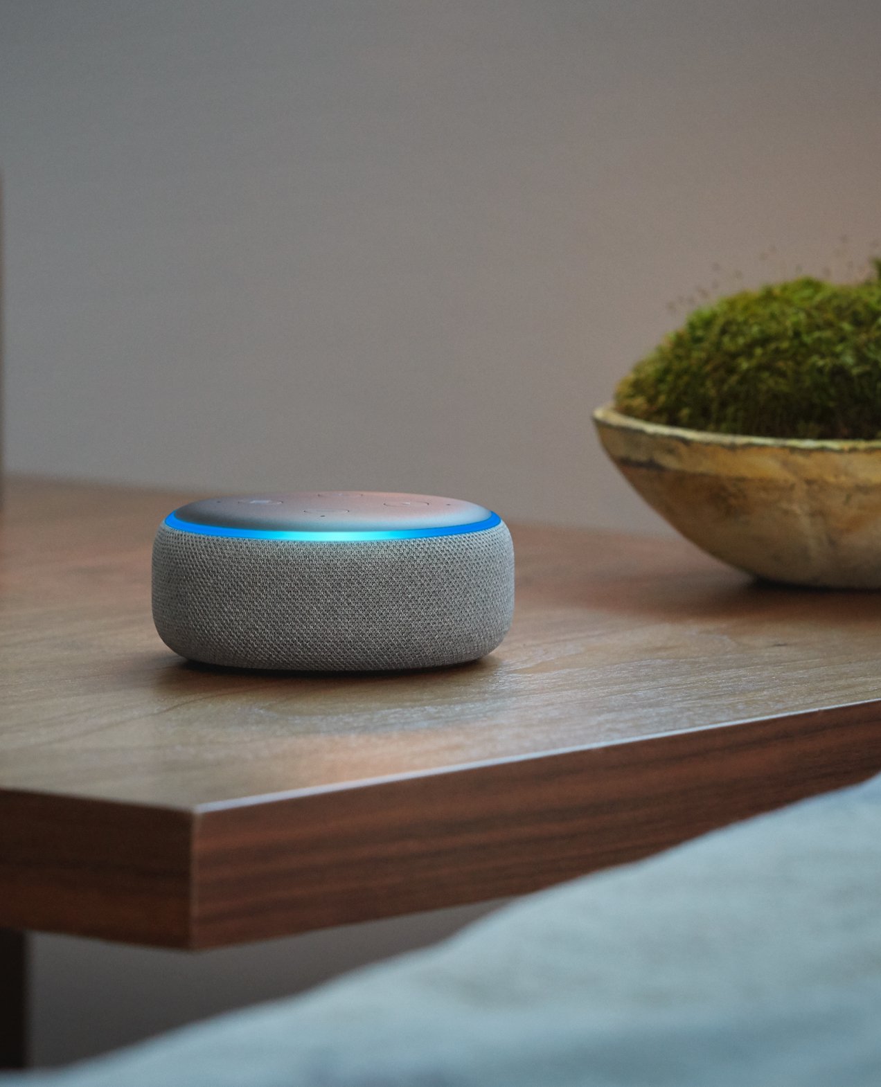 An Amazon Echo smart speaker with a glowing blue ring on a wooden surface.