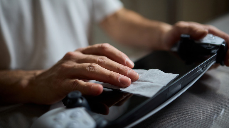 A person using cleaning tools to maintain their gaming hardware and controller.