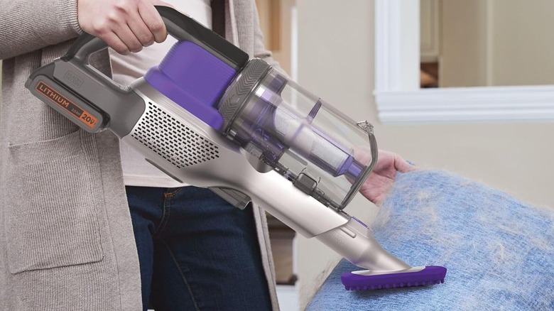 A person using the Black+Decker Powerseries vacuum on a pet hair-covered pillow.
