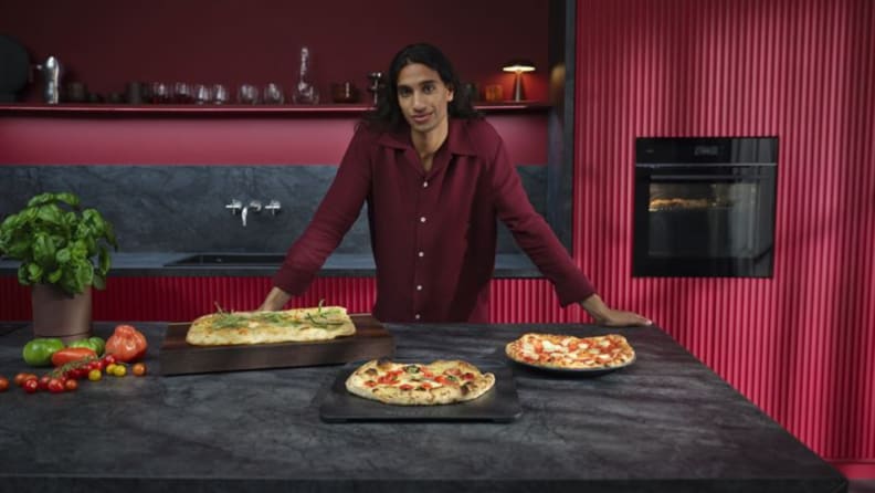 A person pulling a fresh pizza out of a modern AEG smart oven.