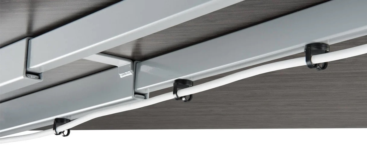 Multiple black UPLIFT magnetic cable clips securing cords to a steel desk frame.
