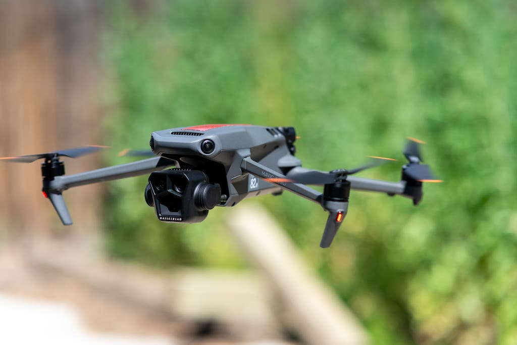 The DJI Mavic 3 Pro, which features a triple-camera system, hovering over a field.