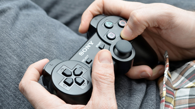 A person holding a DualShock 3 controller and playing a game on a TV screen.