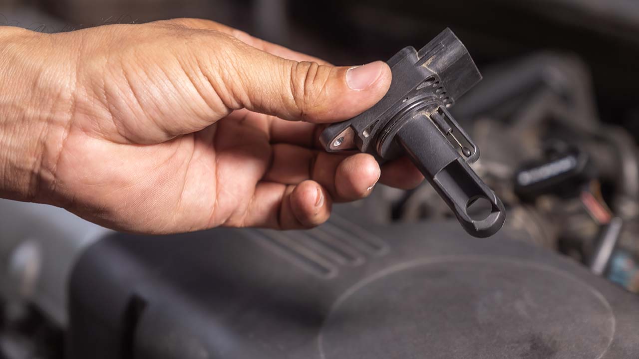 A professional mechanic inspecting a car's air flow meter and engine components.