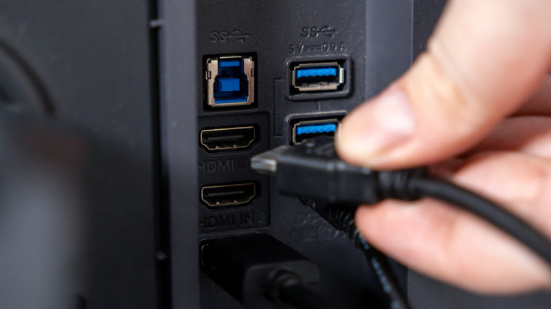 A person connecting an HDMI cable into a modern television's input panel.
