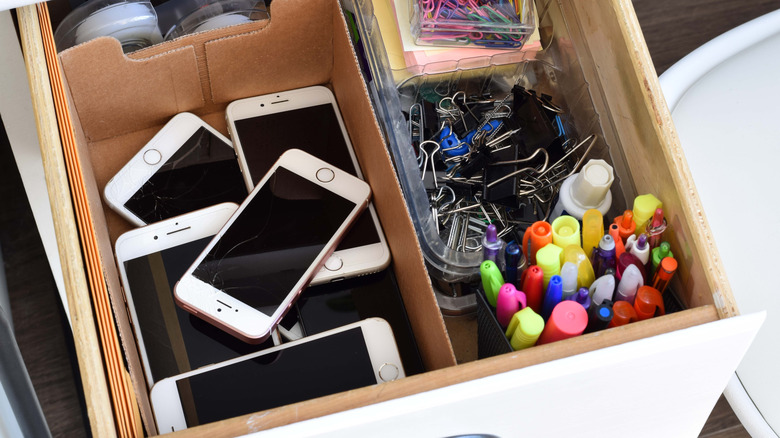A messy drawer filled with loose electronic devices and various stationary supplies.