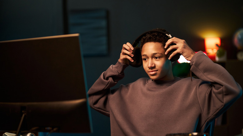 A gamer at a computer desk wearing a brown sweater and adjusting headphones.