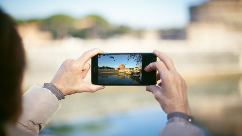 A person holding up a smartphone to photograph the historic Castel Sant'Angelo in Rome.