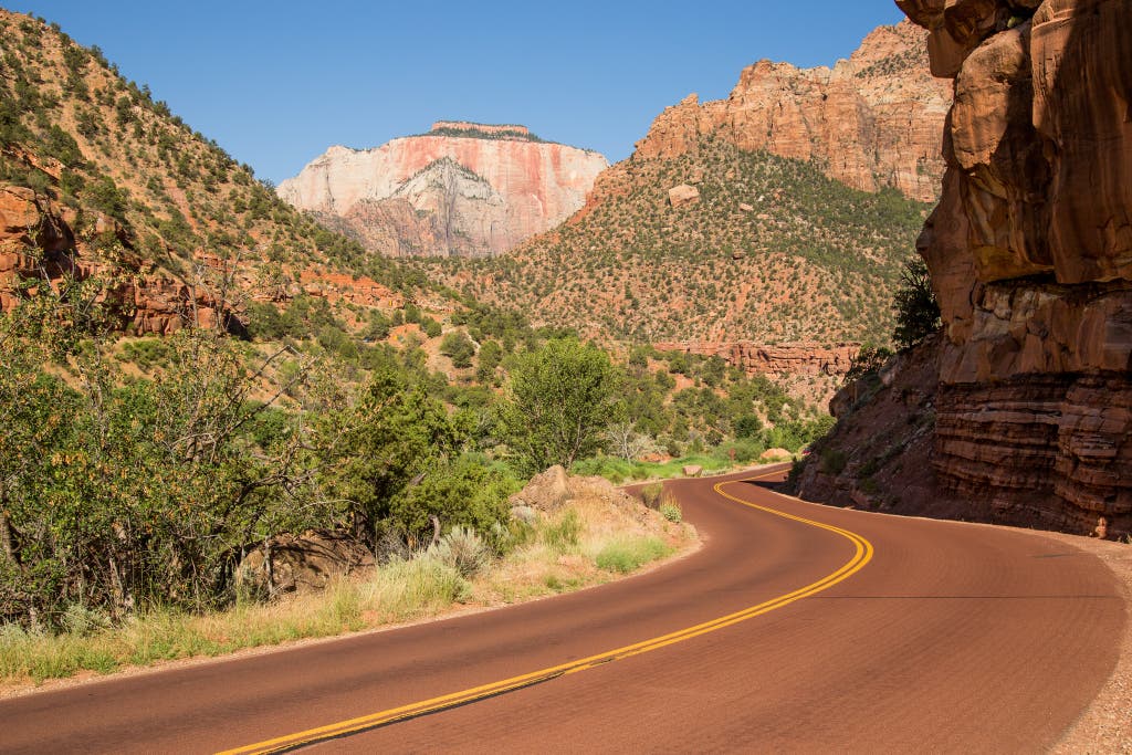 A long, open rural highway stretching through red rock mountains