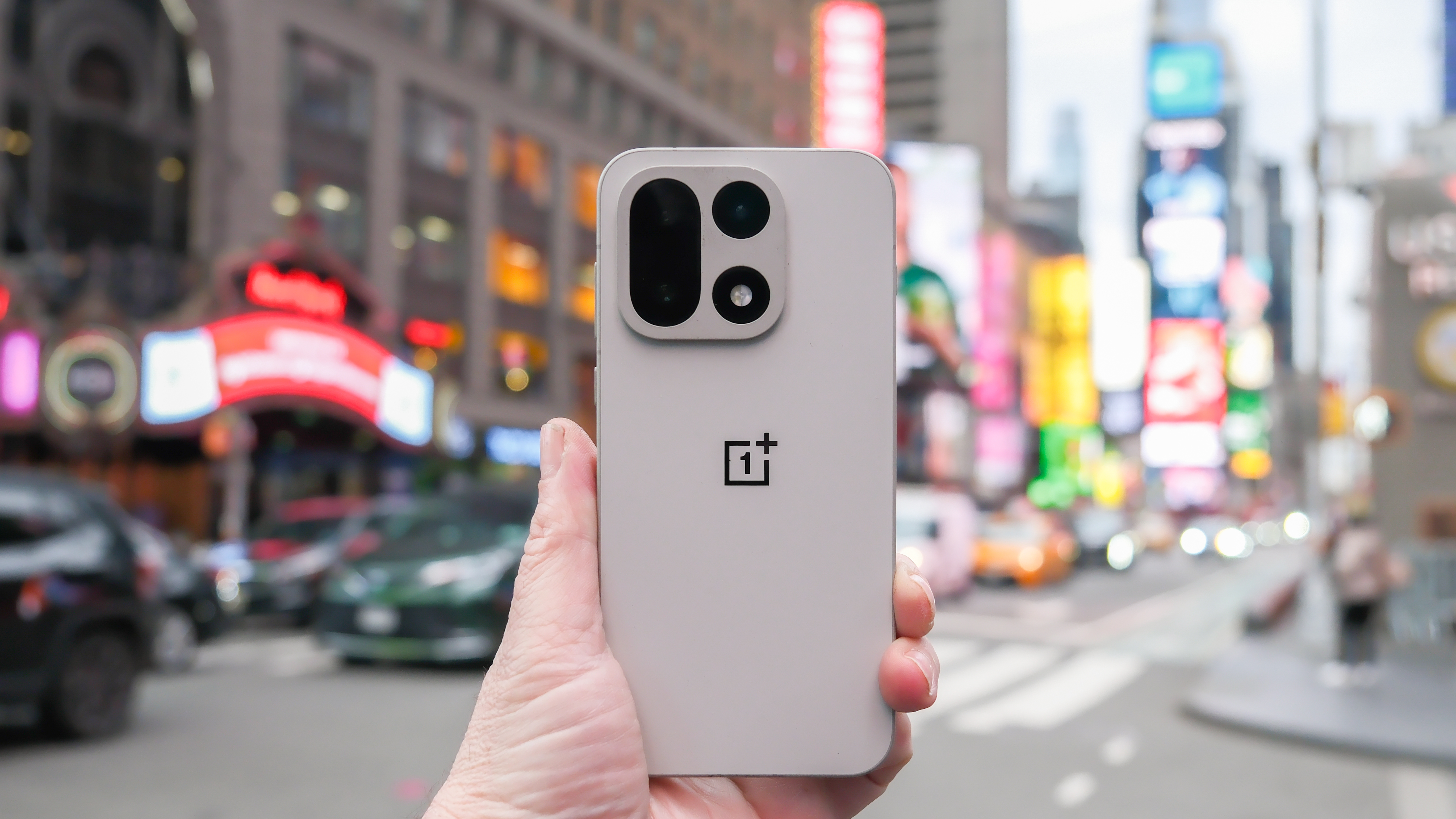A OnePlus phone being held in a busy urban environment at Times Square.