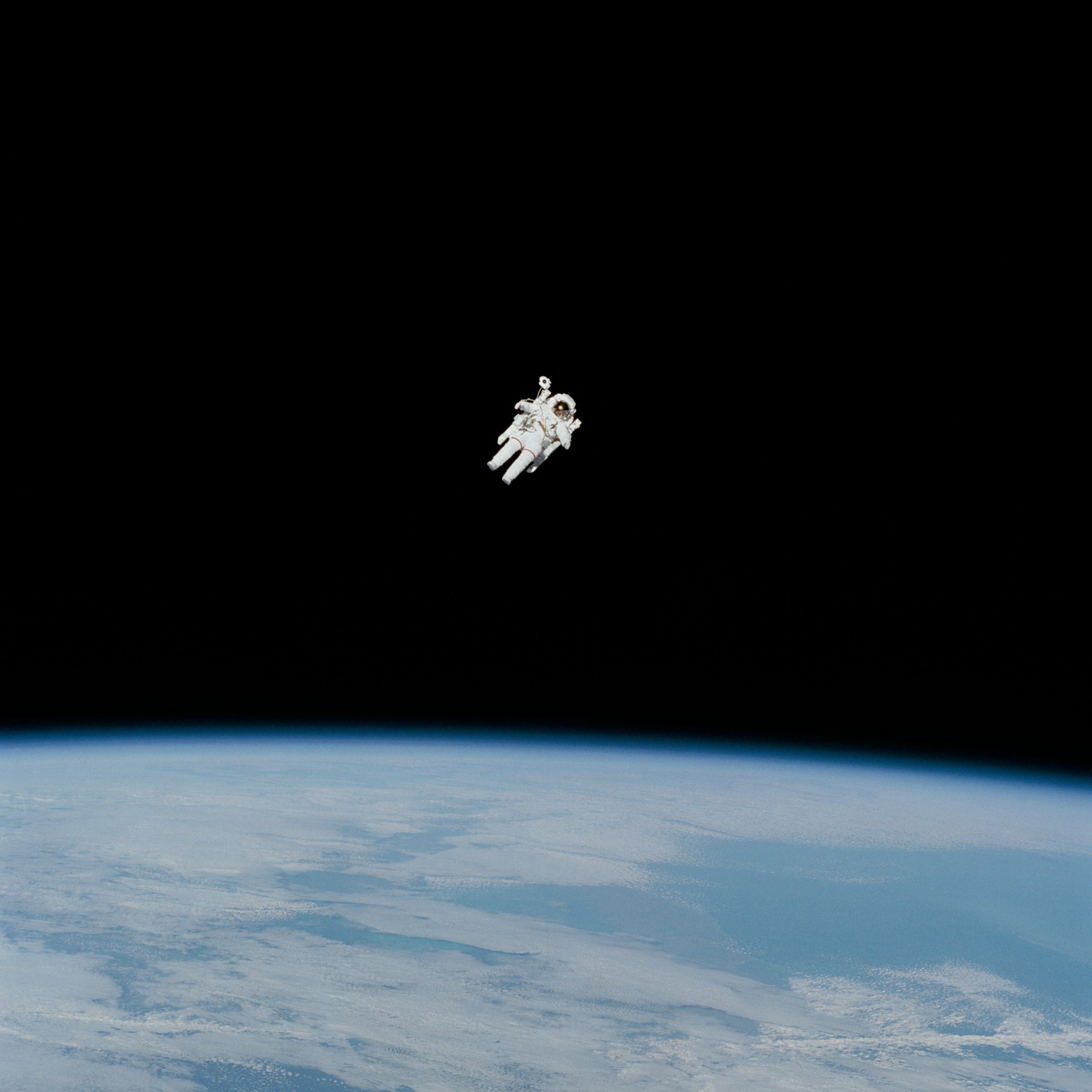 An astronaut in a white spacesuit performing a spacewalk outside a Dragon spacecraft against the blackness of space.