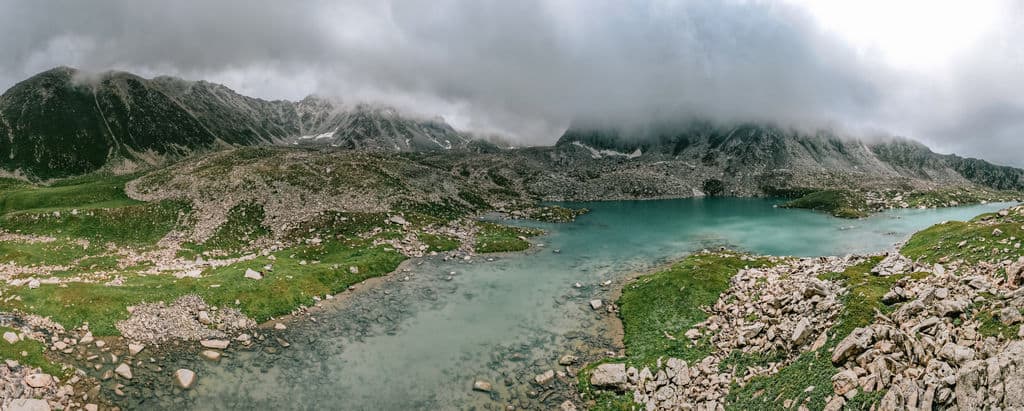 A wide aerial panorama of the blue Chelpek Lakes surrounded by green mountains.
