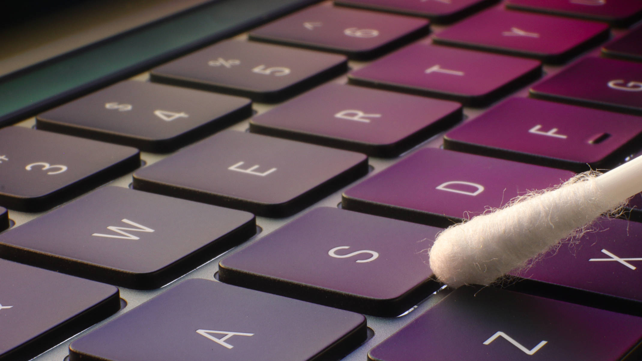 A person using a cotton bud to carefully clean between the keys of a keyboard.